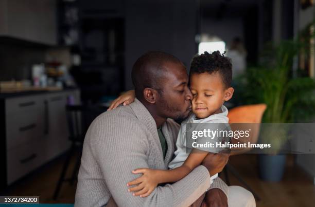 multiracial father embracing and kissing his little son at home - black people kissing stock pictures, royalty-free photos & images