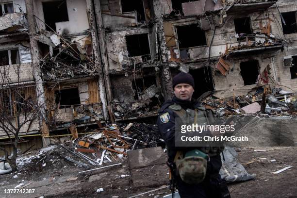 Ukrainian police officer stands in front of a damaged residential block hit by an early morning missile strike on February 25, 2022 in Kyiv, Ukraine....