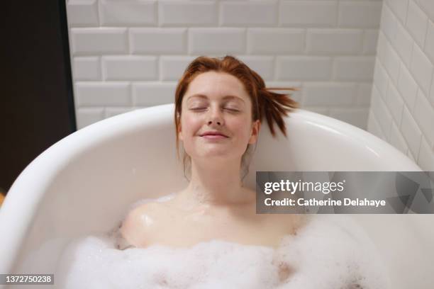 portrait of a beautiful redhead woman taking a bath at home - taking a bath stock-fotos und bilder