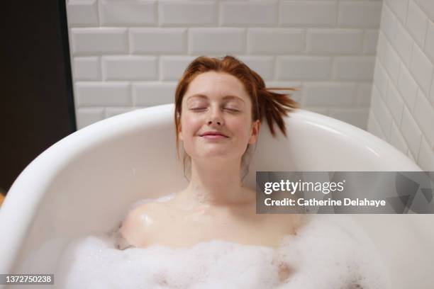 portrait of a beautiful redhead woman taking a bath at home - prendre un bain photos et images de collection