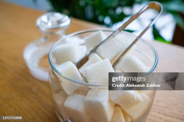 lump sugar in a transparent glass sugar bowl, on a wooden table or background, at home, in a cafe, cafeteria or restaurant. the concept of poor nutrition and lifestyle. - fruchtzucker stock-fotos und bilder