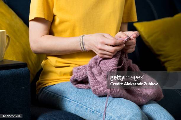 the girl is holding a knitting project and metal knitting needles in close-up. a woman knits a blue wool sweater or scarf, sitting on the couch at home. the concept of hobbies, creativity, needlework and manual work. creating clothes with your own hands. - virada ao contrário imagens e fotografias de stock