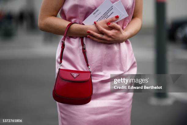 Guest wears a pale pink shiny satin sleeveless midi dress from Prada, a red shiny leather Cleo handbag from Prada, outside the Prada fashion show,...