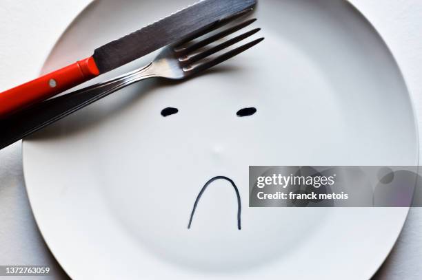 sad face drawn on an empty plate - empty plate stock pictures, royalty-free photos & images