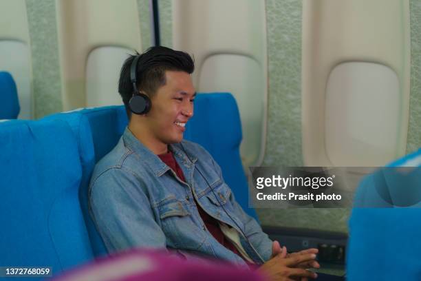 asian passenger traveler man in airplane watching movie or  listening to music on headphones during flight."n - asian cinema stock-fotos und bilder