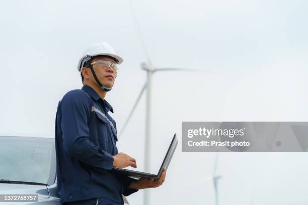 asian man inspection engineers preparing and progress check with laptop of a wind turbine with safety in wind farm in thailand. - asian engineer stock-fotos und bilder