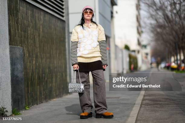 Guest wears a pale pink wool hat, beige sunglasses, silver earrings, a pale yellow wool and white embossed print pattern short sleeves pullover, a...