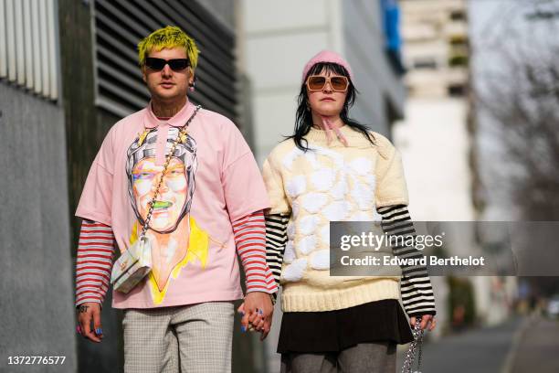 Guest wears black sunglasses, a silver with pink rhinestones earring, a gray and red striped print pattern long sleeves t-shirt, a pale pink with...