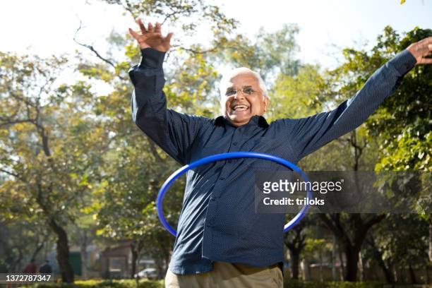 senior man exercising with hula hoop at park - plastic hoop stock pictures, royalty-free photos & images