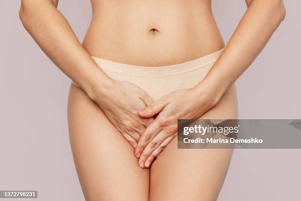 Young woman in underwear holding her crotch with hands, suffering from cystitis on beige background