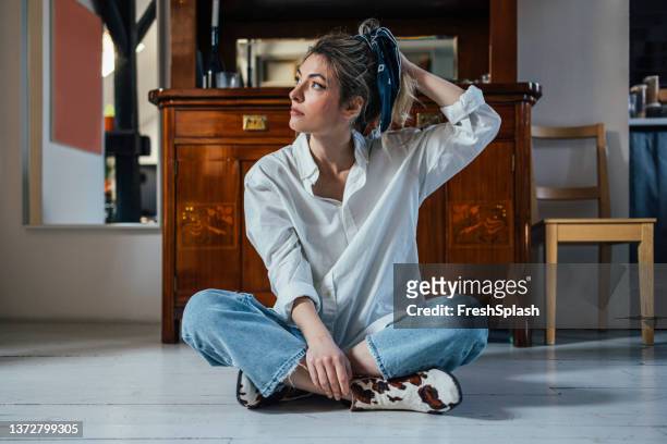 eine schöne kaukasische frau, die auf dem holzboden in ihrem haus sitzt - woman scarf trousers stock-fotos und bilder