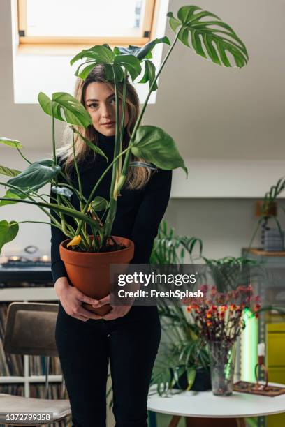 millennials as plant parents: a beautiful caucasian blonde female looking at camera while proudly holding her potted plant - tropical bush stock pictures, royalty-free photos & images