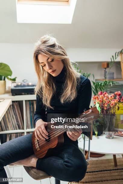 eine schöne kaukasische frau sitzt in ihrer wohnung und spielt ukulele - ukulele stock-fotos und bilder