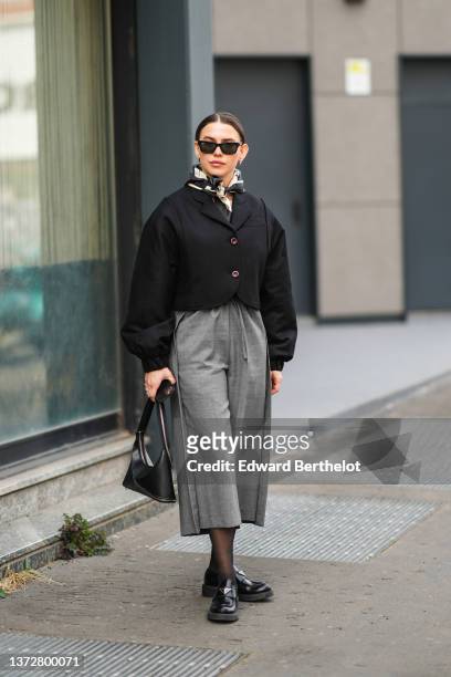 Guest wears black sunglasses from Prada, a gold earrings, a black and beige print pattern silk scarf, a black jacket, high waist gray large shorts, a...