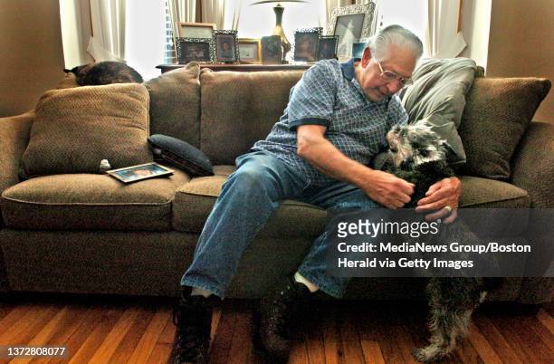Al Cirillo sits on the couch in the living room of his Quincy home Friday as he pets his thirteen year-old dog Katie. A photo of his late wife...