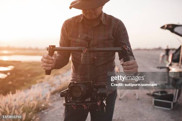 young cinematographer using gimbal stabilizer shooting video footage for content creator of him on the location outdoor - film director asian stock pictures, royalty-free photos & images