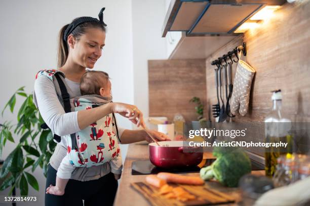 madre multitarea cocinando y cuidando a su hijo recién nacido. - portabebés fotografías e imágenes de stock