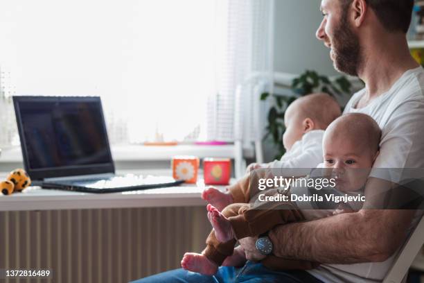 man holding twin babies in his arms when working from home - pure stockfoto's en -beelden