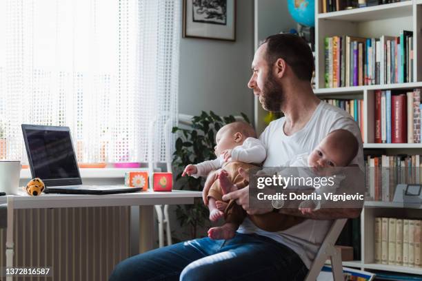 man working during parental leave, holding twin babies and using laptop - pure stock pictures, royalty-free photos & images