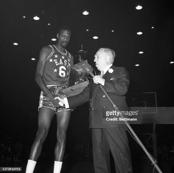 Boston Celtic, Bill Russell grips his Most Valuable Player trophy while being congratulated by the president of the NBA, Maurice Podoloff.