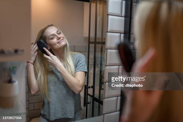 glückliche junge frau, die im badezimmer haare bürstet - brushing hair stock-fotos und bilder