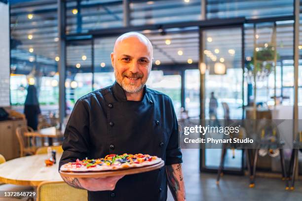 smiling waiter looking at camera and showing a pizza - pizzeria stockfoto's en -beelden