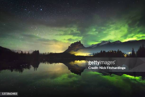 the aurora reflected in a small lake below castle mountain as a train light goes by, banff national park, alberta, canada - banff national park stock-fotos und bilder