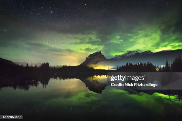 the aurora reflected in a small lake below castle mountain as a train light goes by, banff national park, alberta, canada - banff canada stock pictures, royalty-free photos & images