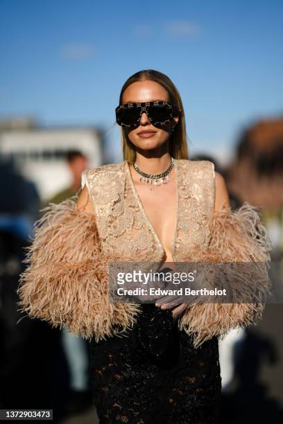 Leonie Hanne wears black and beige monogram print pattern futurist sunglasses from Gucci, silver pendant earrings, a silver chain with letter pendant...