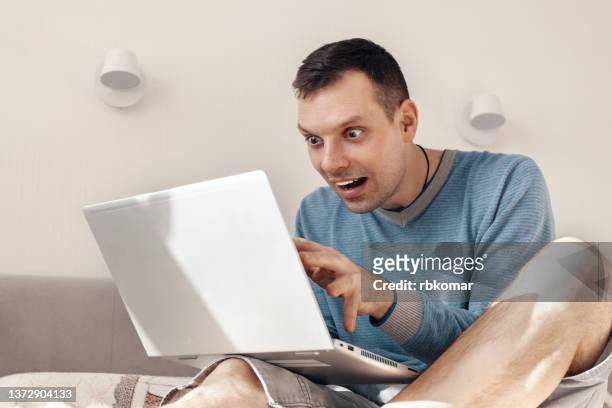 delighted man using laptop computer stretches his hands to the screen and makes a curious face with eyes wide open. internet and social media addiction - euforie stockfoto's en -beelden