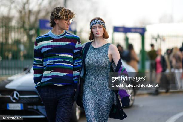 Gavin Casalegno wears glasses, a mint green / purple / burgundy / blue / black military print pattern wool pullover, black checkered print pattern...