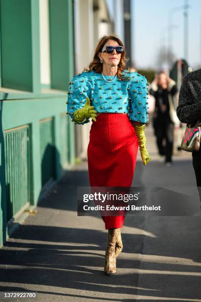 Anna Dello Russo wears black and rhinestones sunglasses from Gucci, rhinestones earrings, a blue sequined with large gold embroidered balls /...