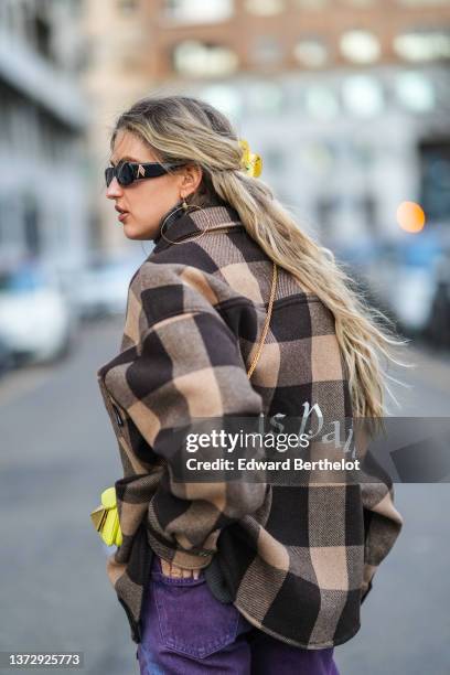 Emili Sindlev wears black sunglasses, gold flower pendant earrings, a dark gray ribbed turtleneck pullover, a beige and dark brown checkered print...