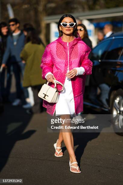 Alexandra Pereira wears white sunglasses, gold earrings, a white long sleeves / square-neck short dress, a pink embossed zipper hoodie coat, a white...