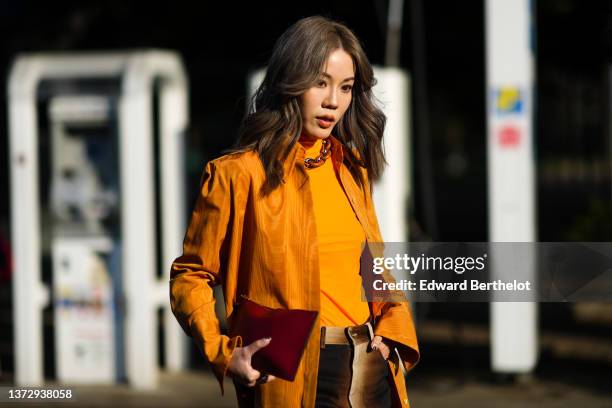 Guest wears silver earrings, a silver and orange large chain necklace, a neon orange turtleneck t-shirt, an orange reflect print pattern shirt, a red...