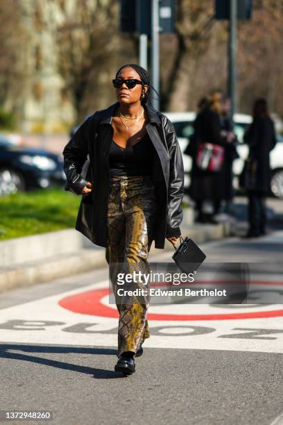Guest wears black sunglasses, gold earrings, gold pendant necklaces, a black V-neck t-shirt, a black shiny leather oversized jacket, a black leather...