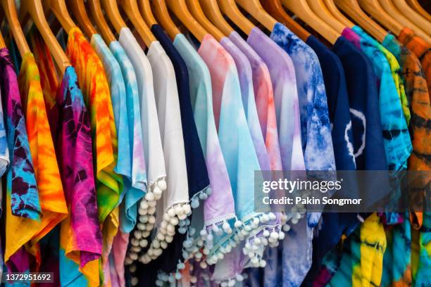 a rack of colorful shirts hangs for sale at a local market in phuket, thailand. - red shirt stock-fotos und bilder