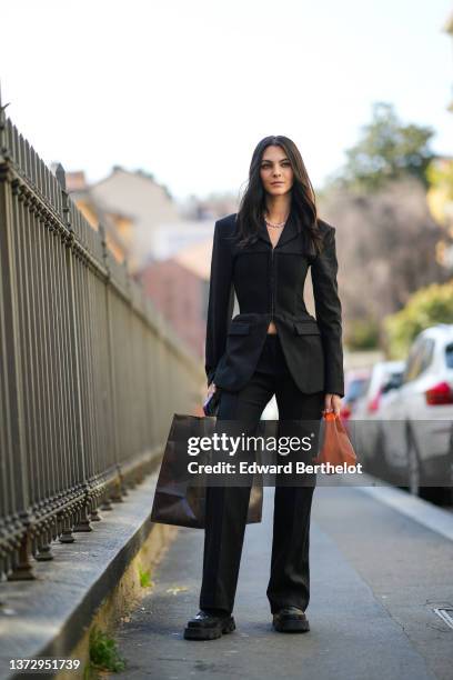 Guest wears a silver chain necklace, a black buttoned corset blazer jacket, high waist matching black suit pants, a neon orange shiny leather...