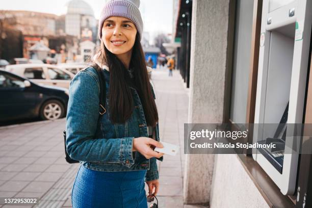 una mujer usa un cajero automático - bank holiday fotografías e imágenes de stock