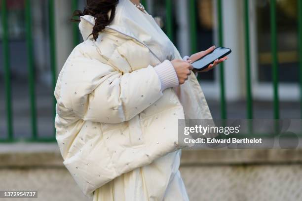 Guest wears a white large pearls necklace, a white latte with embroidered rhinestones oversized puffer jacket, a white latte midi skirt, outside the...