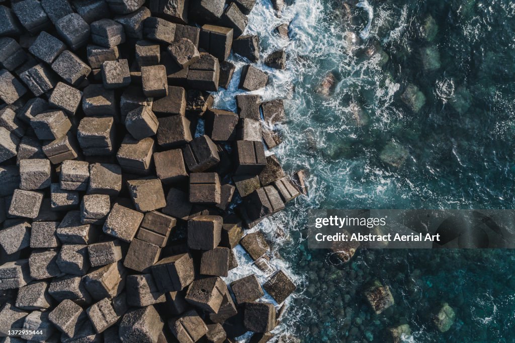 Waves from Atlantic Ocean crashing onto coastal Tetrapods seen from above, Tenerife, Spain