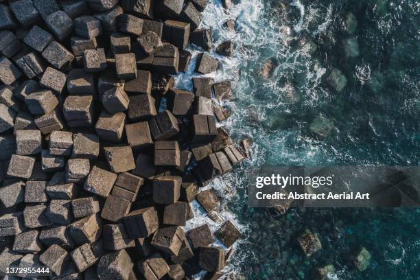 waves from atlantic ocean crashing onto coastal tetrapods seen from above, tenerife, spain - protection stockfoto's en -beelden