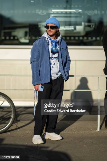 Guest wears a blue ribbed wool beanie, black sunglasses, a pale gray and navy blue print pattern hoodie sweater from Isabel Marant, a gray blue...