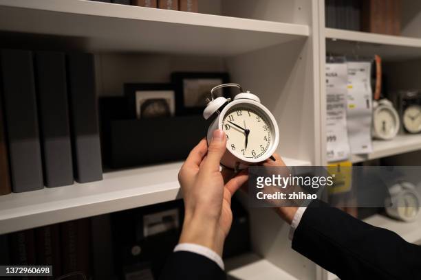 human hand adjusting alarm clock - zeitumstellung stock-fotos und bilder