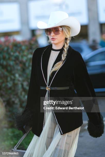 Guest wears a white felt cow-boy hat, sunglasses, a white latte pleated tulle long dress, a black velvet blazer jacket with large feathers wrists, a...