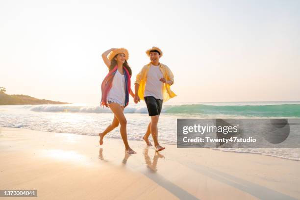 lovely asian couple enjoying summer vacation at the beach in morning - hand in hand spazieren stock-fotos und bilder