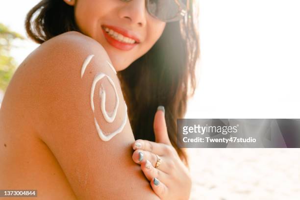 woman in bikini applying suntan lotion on the beach - beautiful woman body stockfoto's en -beelden