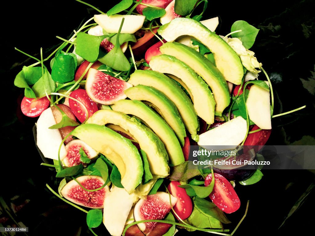 Close-up of fresh salad with slice of avocado, fig, apple, miner's lettuce, tomato