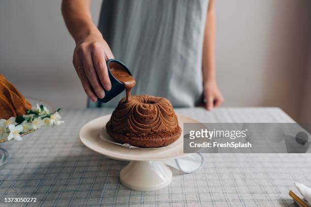 anonymous female pastry chef pouring chocolate frosting over a bundt cake - tulbandcake stockfoto's en -beelden