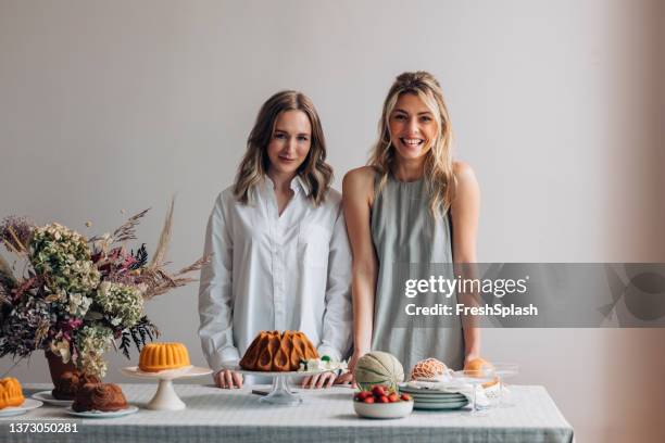 two smiling female friends having fun while setting the table for a birthday party (looking at camera) - sister stock pictures, royalty-free photos & images